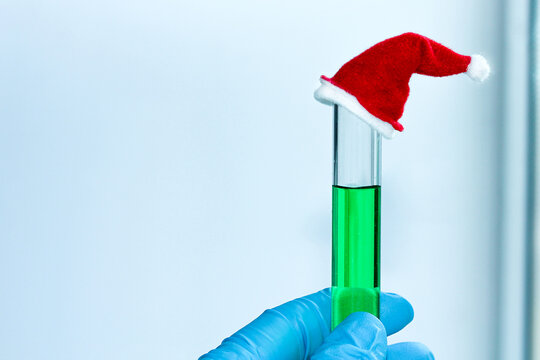 a blue-gloved hand holds a test tube with a green solution with a decorative red cap in the chemical laboratory