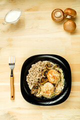 Chicken meatballs with mushrooms in a creamy sauce with green buckwheat in a black plate next to mushrooms and cream.