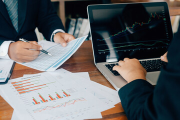 Business team colleagues planning and analyzing graph stock market trading on laptop computer with stock chart data