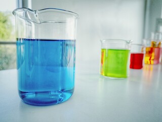 Close up Science glass flask with blue and other colors in water in chemistry research laboratory.