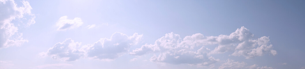 White fluffy clouds on a gentle blue sky in the rays of the sun. Panoramic view. Abstract blue sky background. Clouds in the sunlight.