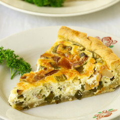 Piece of quiche with chanterelles, herbs and cheese on a white plate