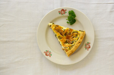 Piece of quiche with chanterelles, herbs and cheese on a white plate