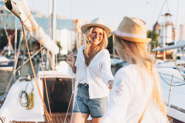 Two beautiful blonde girls friends mother and daughter in white and straw hats on the yacht at the...