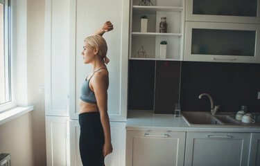 Caucasian blonde lady wearing sportswear is stretching up before doing yoga at home