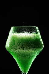 Green drink is poured into a glass. Black background.