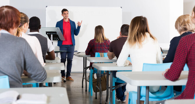 Confident male student answering at whiteboard in front group of students in auditorium.