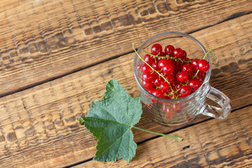 Ripe red currants in glass on wooden background.