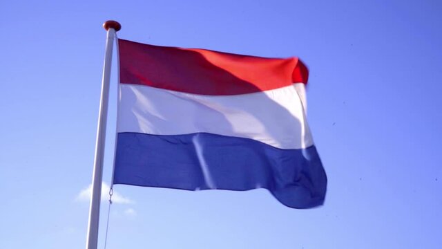 Slow-motion shot of Dutch flag waving in the wind. Blue sky, sunny day.