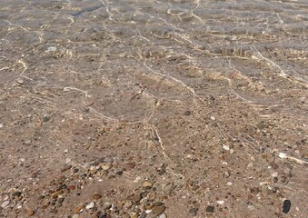 Klares Wasser am Kiesstrand, mit sanften Wellen an der Oberfläche