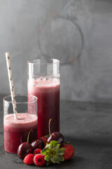 Different type glass with fresh berries smoothie and cherry, strawberry and raspberry fruit on dark background. Perfect drink for vegan and vegetarian diet
