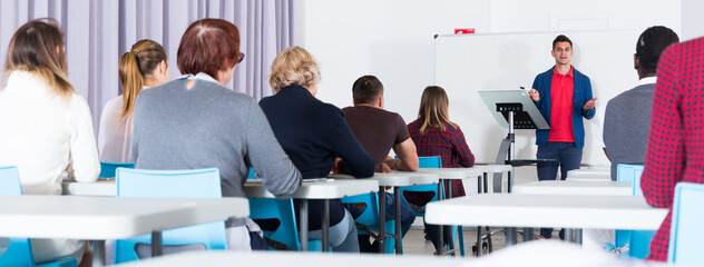 Concentrated adult students of different nationalities with teacher studying in classroom