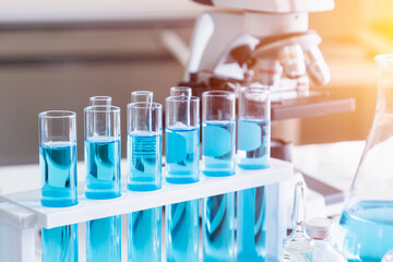 Test tubes with blue liquid in holder with microscope in background. Science glass equipment in laboratory for chemistry and medical research.