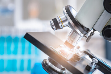 Close-up of microscope examining slide of sample with test tubes in background. Concept for science and technology research in laboratory.