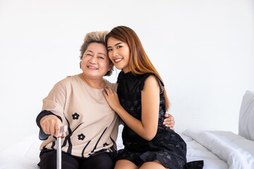 Obraz premium Happy senior elderly Asian woman female mother holding cane with daughter sitting on bed in bedroom, looking at camera
