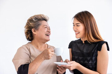 Happy daughter woman serving giving coffee tea cup drink to senior elderly Asian woman female mother sitting on bed in bedroom