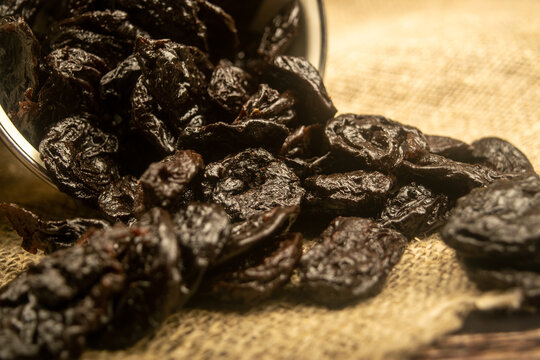 Dried prunes spilled from a metal bowl on a wooden background. Close up.