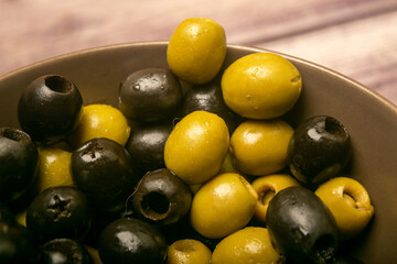 Green olives and black olives in a ceramic bowl on a wooden background. Close up.
