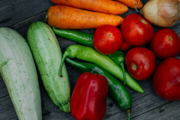 A variety of fresh vegetables, tomatoes, onions, zucchini, carrots, red and green peppers, on a rustic wooden table.