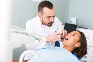 male Dentist is treating patient which is sitting in dental chair in clinic