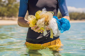 Man collects packages from the beautiful turquoise sea. Paradise beach pollution. Problem of...