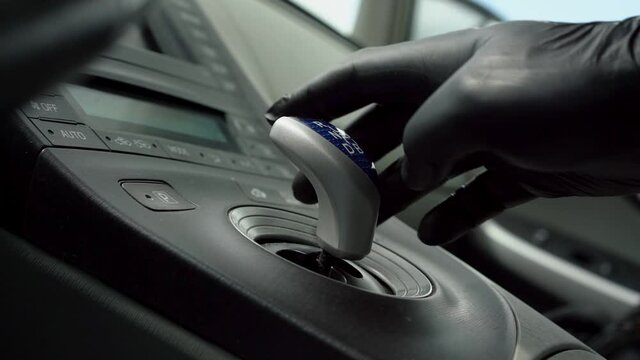 person in black glove hand moves blue and grey gear stick near dashboard of new automobile slow motion close view