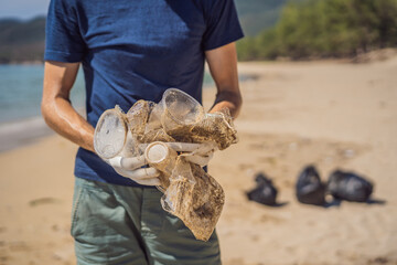Man in gloves pick up plastic bags that pollute sea. Problem of spilled rubbish trash garbage on the beach sand caused by man-made pollution and environmental, campaign to clean volunteer in concept
