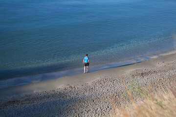 Hombre solitario en pantalón corto, en la orilla del mar, con camiseta azul, mirando el agua, en un día soleado en la costa del sol.