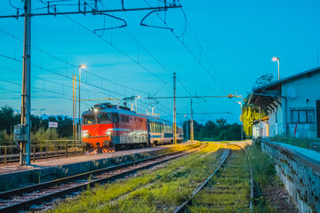 Fototapeta na wymiar Passenger train hauling classical passenger coaches at night on a station of Preserje in Slovenia. Evening setting of an older type of train.