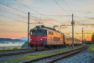 Obraz na płótnie Canvas Night passenger train from Prague to Rijeka on its way over the Ljubljana marshes in early romantic morning with sunrise. Fast overnight express to Dalmatia.