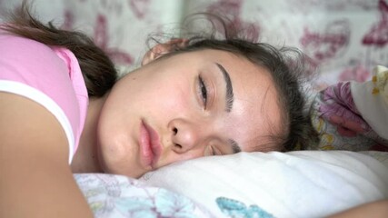 sleeping teenager girl with long hair wakes up opens and closes eyes lying on large bed at home in early morning closeup - Powered by Adobe