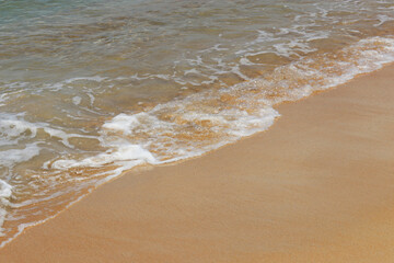 Surf on a sandy beach for background, empty sea coast with yellow sand and clear water, wave with white foam