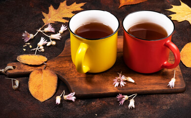 colored cerom tea cups, autumn maple leaves on a rusty brown background