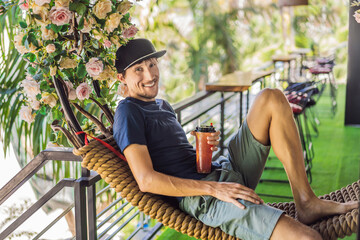 Obraz na płótnie Canvas Young man drinks summer fruit drink on a summer terrace