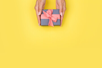 Top view of female hands holding a present box package in palms, on yellow background