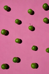 Green plum isolated on pink background. Still life photography.	