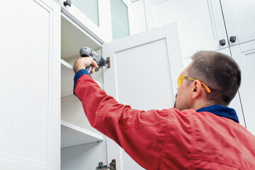 Obraz premium Worker using cordless screwdriver while installing new furniture in kitchen
