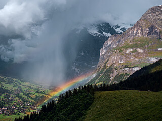 Aerial shot of a rainbow breaking behind a storm cloud in the alpine valley of Grindelwald in Switzerland.