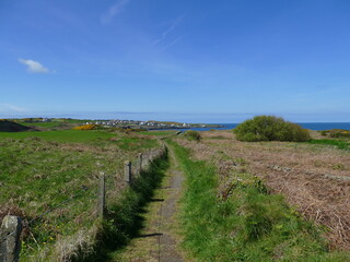 Coastal footpath running down towards the sea with barbed wire fence and blue sky