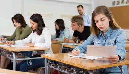 Fototapeta premium Young girl is writing test and thinking about questions at the desk in the class.