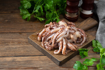 The tentacles of squid. Raw squid tentacles on a wooden serving Board on a brown wooden kitchen table. Lots of squid tentacles