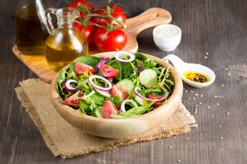 Fresh healthy vegetable salad made of cherry tomato, ruccola, arugula, feta, olives, cucumbers, onion and spices. Greek, Caesar salad in a white bowl on wooden background. Healthy food concept.