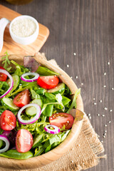 Fresh healthy vegetable salad made of cherry tomato, ruccola, arugula, feta, olives, cucumbers, onion and spices. Greek, Caesar salad in a white bowl on wooden background. Healthy food concept.