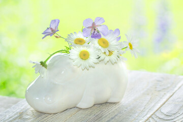 On a Sunny day on a light wooden background is a vase in the form of a Hippo with wild flowers