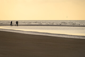 Three people stroll on the beach in the late afternoon.