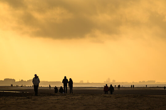 Silhouettes of people on the beach at sunset under cloudy sky.