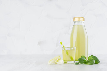 Fresh vegetable green spinach and celery juice in glass bottle mock up with glass, straw, stems, leaves in soft light white interior on wood table.