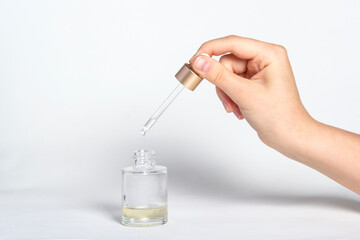 Pipette dropper with drop of natural oil above glass bottle on white background. Natural organic skin care beauty products.