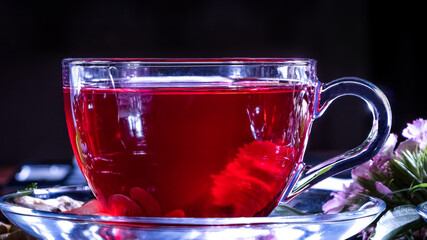 A mug of red tea in white hibiscus flowers and green leaves of medicinal tea on a wooden stand.Zen tea ceremony. Photo of red herbal Indian healing tea. Elegant mugs with a relaxing and tonic drink