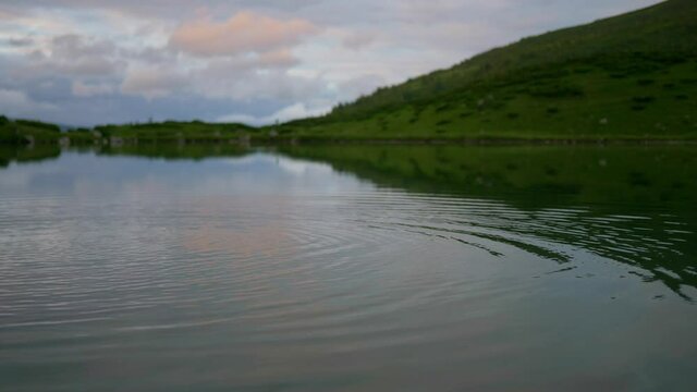 beautiful mountain lake with skipping stone, clear water reflecting sky and stone thrown in water making ripples, pure environment, zen landscape